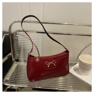 Dettaglio borsa baguette in pelle verniciata rossa con fiocco dorato e zip a fiore