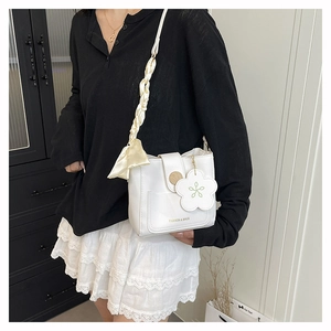 Detail of white leather crossbody bag with silk scarf handle and floral charm accessory