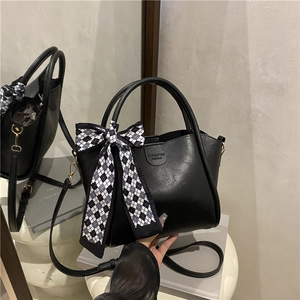Minimalist black leather bucket bag with checkered bow charm and adjustable strap