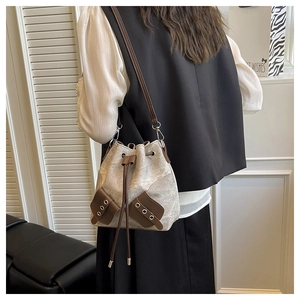 Detailed side view of a beige canvas bucket bag with brown leather trim and drawstring strap