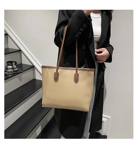 Detailed side view of khaki tote bag with brown straps worn by a model on stairs