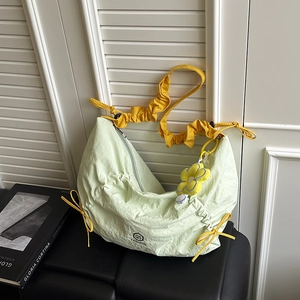 Light green nylon crescent crossbody bag with yellow ruffled strap and floral charm