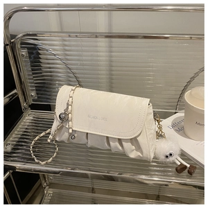 Détail d'un sac bandoulière plissé beige avec breloque peluche et chaîne en métal