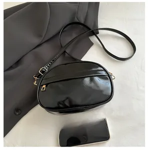 Detail of black oval crossbody bag in patent leather with gold hardware and phone reference