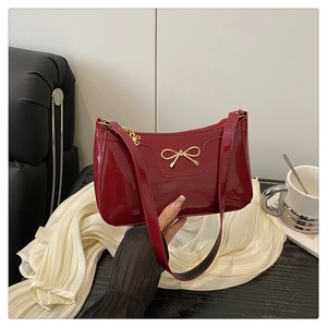 Dettaglio borsa baguette in pelle verniciata bordeaux con fiocco in metallo dorato