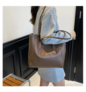 Detail view of large brown tote bag showing side stitching and slim shoulder straps