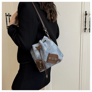 Detail of blue denim bucket bag with brown leather trim worn by model in suit