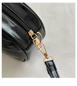 Detail of glossy black shell bag featuring premium gold hardware and smooth zipper