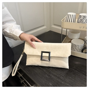 Close-up of cream envelope clutch bag featuring a matte black square buckle and wrist strap