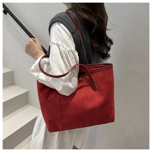 Model wearing a large red suede tote bag with metal logo detail in a minimalist stairway