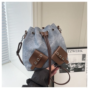 Detail of washed denim bucket bag with leather drawstring and metal eyelet pockets