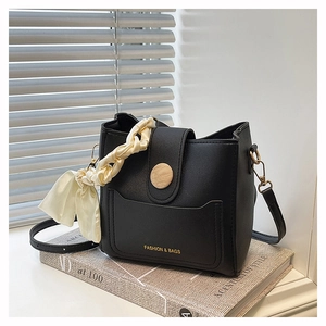 Close-up of black leather bucket bag featuring a wood-grain buckle and silk scarf accent
