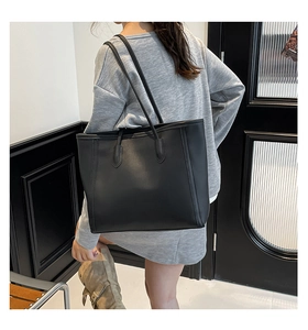 Lifestyle shot of a black minimalist leather tote bag worn as a shoulder bag
