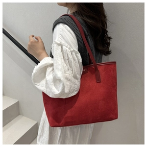 Close-up of a red suede tote bag with slim shoulder strap worn by a model in casual style