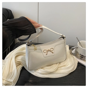 Dettaglio di borsa bianca in vernice con fiocco dorato e pendente floreale