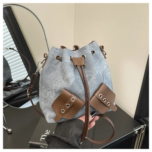 Detail of blue denim bucket bag featuring brown leather trim and metal eyelet pockets