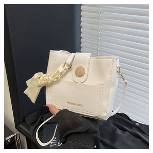 Detail of cream bucket bag featuring a round wood-grain clasp and elegant silk scarf accessory