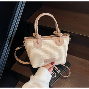 Detail of woven straw handbag with pink leather trim and knotted handle on wooden steps