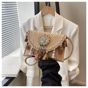Dettaglio della borsa a busta in paglia boho con nappe e ciondolo mandala di perline