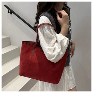 Detail of red suede tote bag worn on shoulder by model against a minimalist background