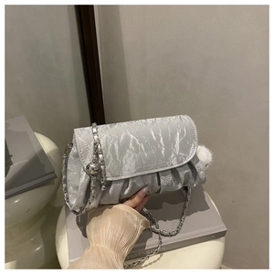 Gros plan d'un sac bandoulière argenté plissé avec chaîne et détail de breloque sphérique