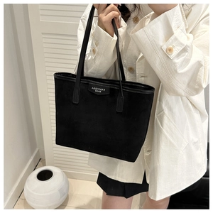Close-up of minimalist black suede tote bag featuring long handles and elegant leather tag