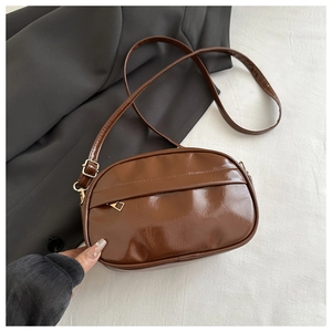 Close-up of dark brown oval crossbody bag featuring glossy patent leather and gold zipper