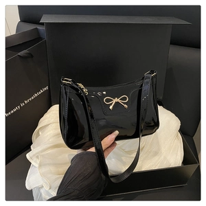 Dettaglio borsa hobo in vernice nera con fiocco dorato e confezione regalo di lusso
