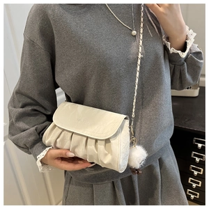 Detail of a creamy white pleated crossbody bag with a metal chain and fuzzy pompom accessory