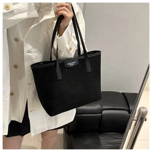 Close-up of black suede tote bag with brand logo patch and slim leather straps