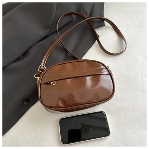 Top view of a brown glossy crossbody bag with adjustable strap next to a smartphone