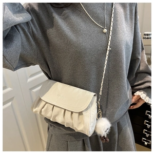 Detail of white pleated crossbody bag with chain strap and cute plush monster charm