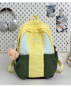 Close-up of color-block nylon backpack featuring blue yellow green panels and bear charm