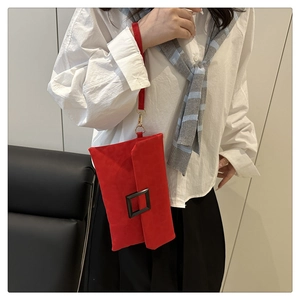 Detail of red suede envelope clutch with a large black square buckle and wrist strap