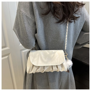 Close-up of white pleated crossbody bag with metal chain strap and a fuzzy monster charm