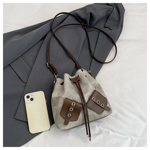 Detail of canvas bucket bag showing drawstring closure and brown leather pocket accents