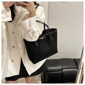 Mirror selfie showing a black canvas tote bag with leather straps and a logo patch