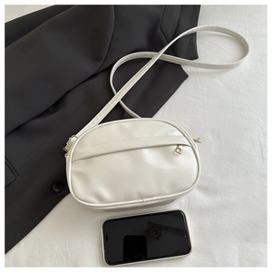 Close-up of white crossbody bag next to a smartphone showing compact internal size and texture