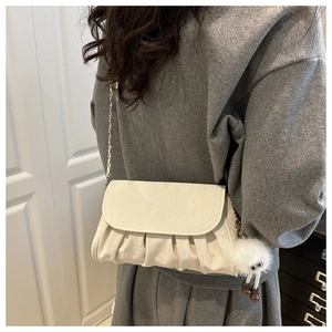 Close-up of cream pleated shoulder bag with gold chain strap and plush charm detail