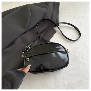 Overhead shot of black patent leather oval crossbody bag with gold zipper detail