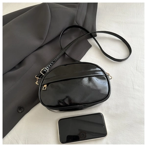 Close-up of black glossy patent leather crossbody bag with golden zipper and adjustable strap