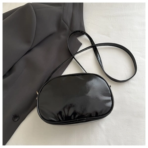 Flat lay of glossy black patent leather oval crossbody bag on gray blazer background