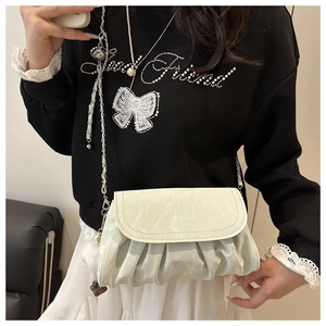 Detail of light green pleated crossbody bag with silver chain strap and pompom charm