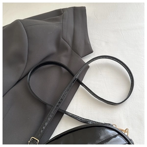 Close-up of black patent leather crossbody bag with gold buckle on a suit background