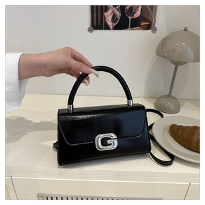 Detailed shot of the silver diamond G buckle on the black shiny leather handbag