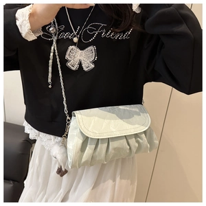 Close-up of mint green pleated crossbody bag with silver chain and plush charm pendant