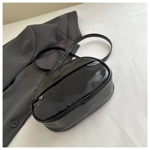 Detailed close-up of a black glossy crossbody bag on white textured fabric background