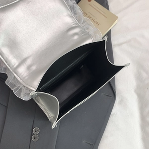 Borsa a mano quadrata in PU argento con pizzo bianco posata su un blazer grigio