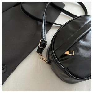 Detail of glossy black faux leather crossbody bag with polished gold-tone hardware buckles