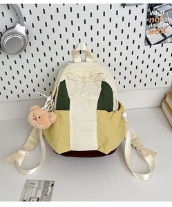 Detail of multi-color nylon backpack with bear keychain and embroidery on white desk